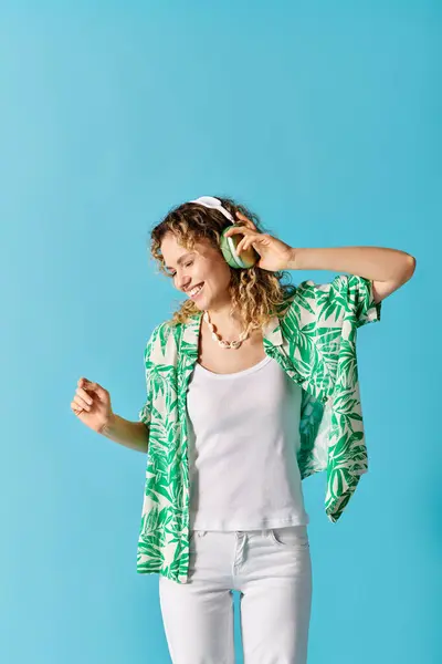 stock image Stylish woman in green shirt and white pants, listening to music.