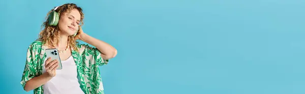 stock image Curly-haired woman in headphones enjoying music on blue backdrop.