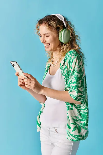 stock image Curly-haired woman wearing headphones, listening to music on her phone.