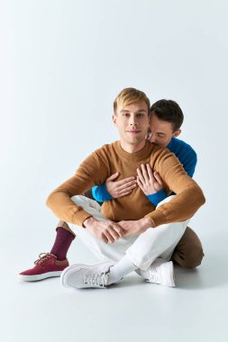 Two men sit closely, embracing each other with arms around, conveying love and connection. clipart
