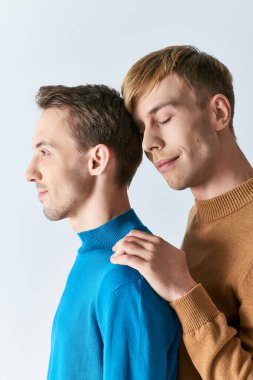 A man tenderly helping another man put on his sweater, showcasing love and support. clipart