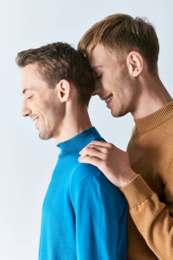 İki adam, birbirini seven eşcinsel bir çift, gri bir arka planda günlük giysiler içinde yan yana dururlar..