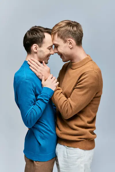 stock image Two men in casual attire embrace each other, standing side by side against a gray backdrop.