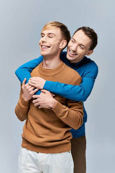 Two men in casual attire hugging each other with smiles.