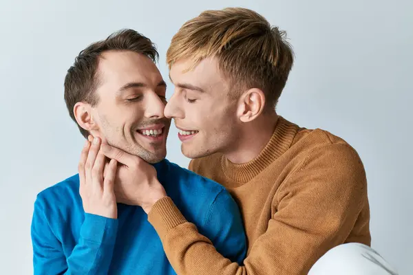 グレーの背景に暖かい抱擁を共有するカジュアルな服装で愛するゲイカップル — ストック写真