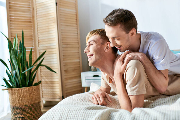 Two men dressed casually, lying together on a bed.