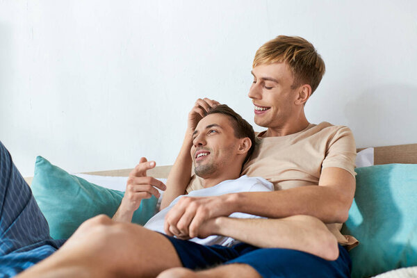 Двое мужчин в повседневной одежде сидят вместе на кровати.