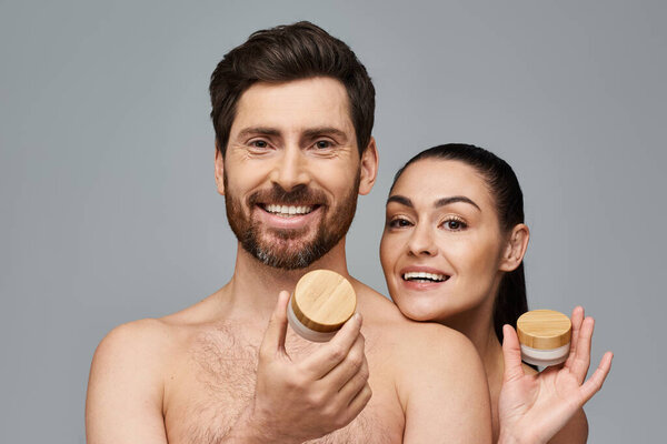 A man and a woman elegantly hold a jar of cream, showcasing their skincare routine.