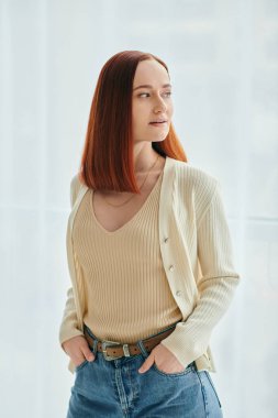 A redhead woman pending quality time in a modern apartment. The woman is wearing jeans and a white cardigan. clipart