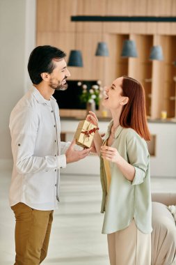 Güzel bir yetişkin çift, kızıl saçlı bir kadın ve sakallı bir adam, modern bir apartman dairesinde hediyelerini değiş tokuş ediyorlar..