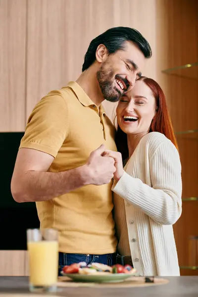 stock image A redhead woman and bearded man stand in their modern kitchen, enjoying quality time together while preparing a meal.