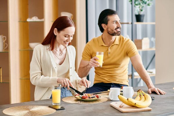 A redhead woman and bearded man enjoy a leisurely breakfast together in their modern kitchen.