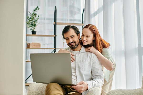 A redhead woman and a bearded man are relaxing on a couch, engrossed in the screen of a laptop.