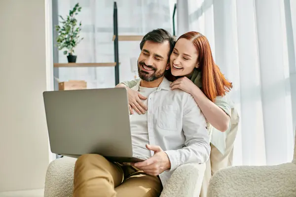 stock image Adult couple, redhead woman and bearded man, enjoy quality time together while sitting on a couch and using a laptop.