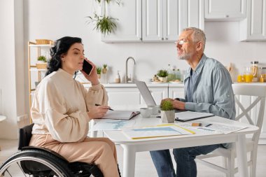 Bir erkek ve kadın bir masada oturur, dizüstü bilgisayara odaklanır, evlerindeki mutfaklarında işbirliği içinde çalışırlar..