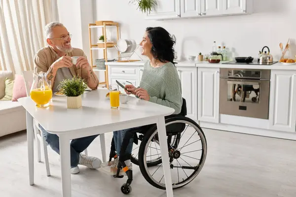 stock image A man in a wheelchair engaged in conversation with a woman in a wheelchair in a cozy kitchen setting at home.
