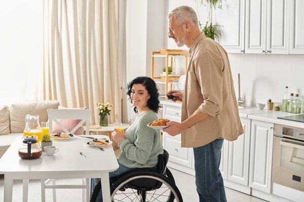 A disabled woman in a wheelchair and her husband preparing a meal together in their kitchen at home.