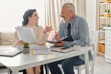 A man and a disabled woman in a wheelchair sit at a table, engaged in deep conversation in their kitchen at home. clipart