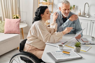 A man and a wheelchair-bound woman planning family budget together at their kitchen table at home. clipart