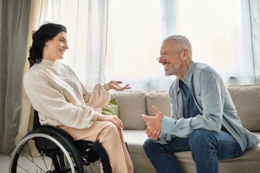 A man converses with a disabled woman in wheelchair in a cozy living room setting. clipart
