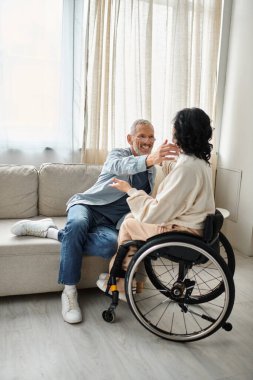 A man and a disabled woman hugging each other affectionately in a cozy living room. clipart