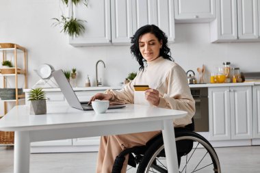 Tekerlekli sandalyedeki engelli bir kadın mutfaktaki dizüstü bilgisayarıyla çalışıyor..