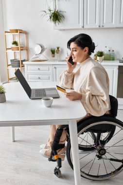 Tekerlekli sandalyedeki engelli bir kadın mutfaktan uzakta çalışıyor, cep telefonuyla konuşuyor..