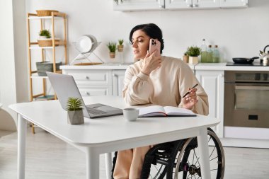 Woman in wheelchair working remotely, chatting on cell phone in kitchen. clipart