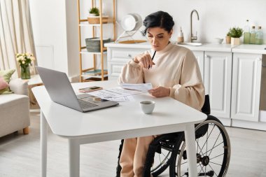 Tekerlekli sandalyedeki engelli bir kadın mutfaktaki dizüstü bilgisayarında çalışıyor. Bağımsızlık ve uyum sağlama yeteneğini gösteriyor..