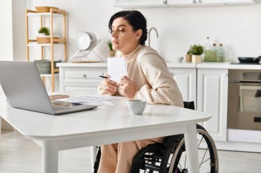 A disabled woman in a wheelchair working remotely on her laptop from her kitchen. clipart