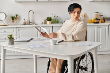 Tekerlekli sandalyedeki engelli bir kadın mutfak masasında tablet kullanıyor..