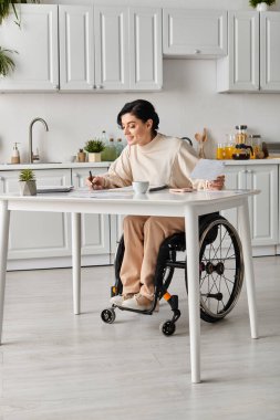 Tekerlekli sandalyede sakat bir kadın mutfak masasında çalışıyor..