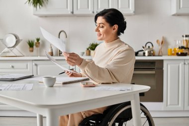 A disabled woman in a wheelchair sits in her kitchen, holding a piece of paper while working remotely. clipart
