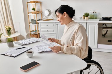 A disabled woman in a wheelchair, engrossed in reading a paper while sitting at a table in her kitchen. clipart