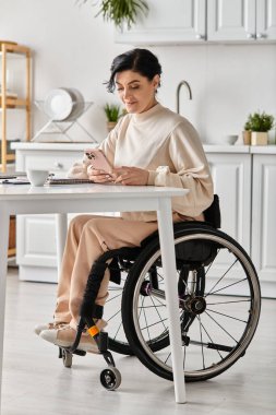 Tekerlekli sandalyedeki engelli bir kadın, bilgisayarını kullanarak mutfaktan uzakta çalışır..