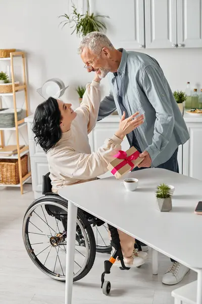 一位坐在轮椅上的残疾妇女在家里的厨房里亲切地挽着丈夫的手 接受着礼物 — 图库照片