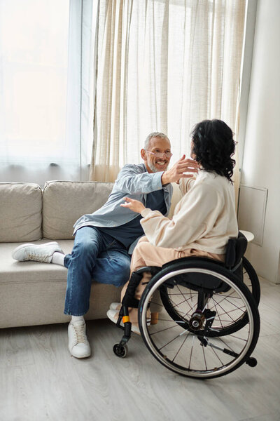 A man and a disabled woman hugging each other affectionately in a cozy living room.