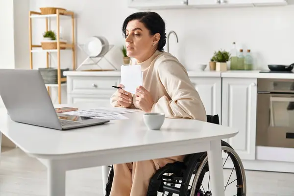 一名坐在轮椅上的残疾妇女在厨房的笔记本电脑上远程工作 — 图库照片