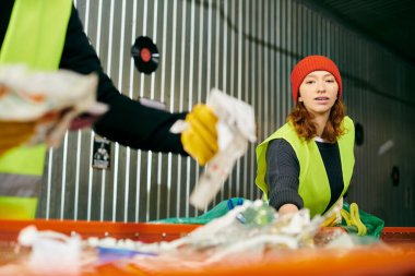 Young volunteer in green vest and red hat sorts trash with eco-conscious peers.