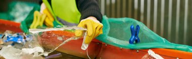 A conscientious young volunteer in a green vest and yellow gloves sorts trash with other eco-conscious individuals.