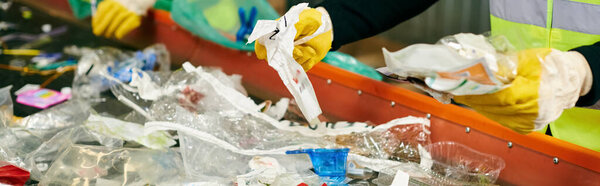 A person in a yellow safety vest collecting plastic bottles, along with young volunteers, sorting trash for recycling.