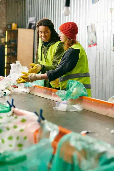 stock image Two young volunteers in gloves and safety vests sorting trash, standing together.