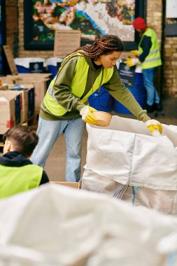A woman in a green jacket helps sort trash with young volunteers in gloves and safety vests. clipart