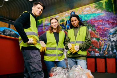 A group of young volunteers in safety vests and gloves sorting trash next to a trash can.