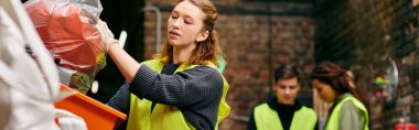 A young woman in a yellow vest picks up discarded items while volunteering with fellow eco-conscious individuals.