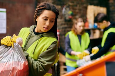 A young woman in a green vest and gloves holding a bag of garbage, participating in a trash sorting activity with other eco-conscious volunteers.