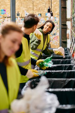 Young volunteers in gloves and safety vests sort through trash at a table filled with waste during a community clean-up event.