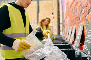 A young man in a yellow vest cleans up trash with other volunteers, promoting environmental consciousness.
