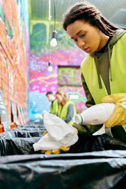 A young volunteer in gloves sorts trash with other eco-conscious people in safety vests.