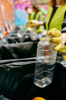 A young volunteer in gloves and a safety vest holds a plastic bottle, promoting eco-conscious actions.